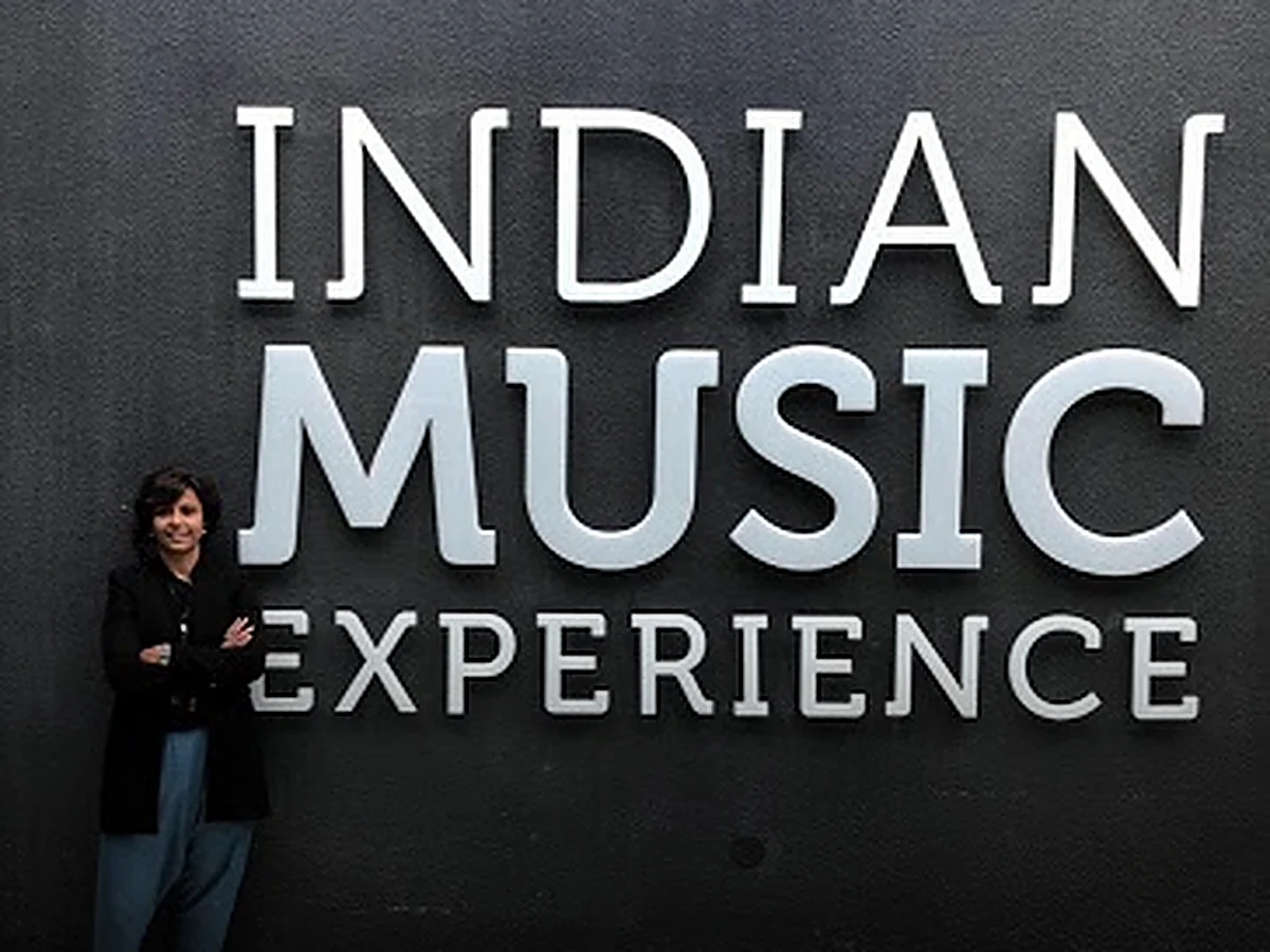 Upasana Nattoji Roy standing with arms crossed in front of the large Indian Music Experience wall lettering