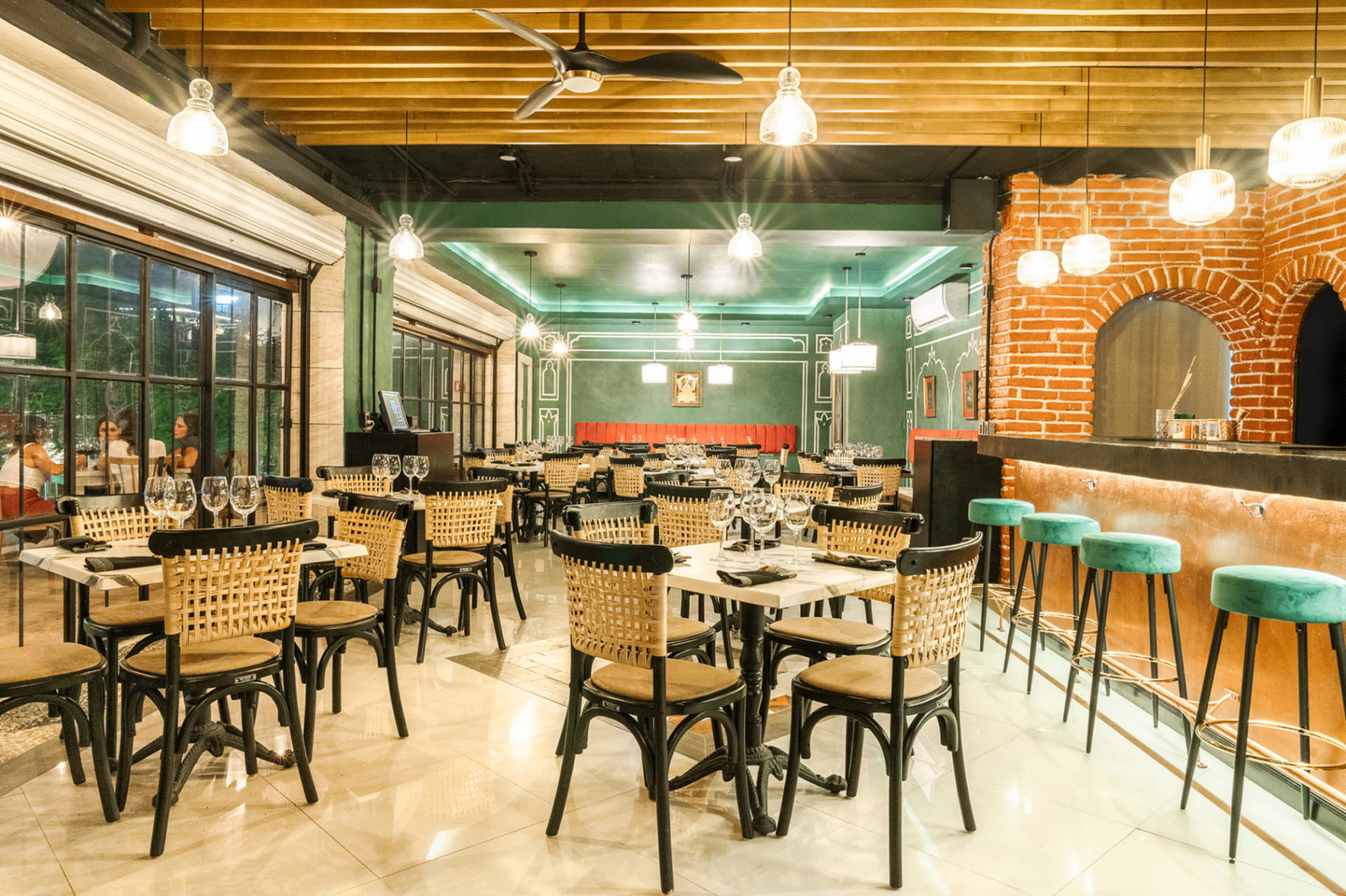 India Jones - Restaurant interior showcasing teal walls, orange brick pizza oven, wicker chairs, and pendant lighting in Playa del Carmen
