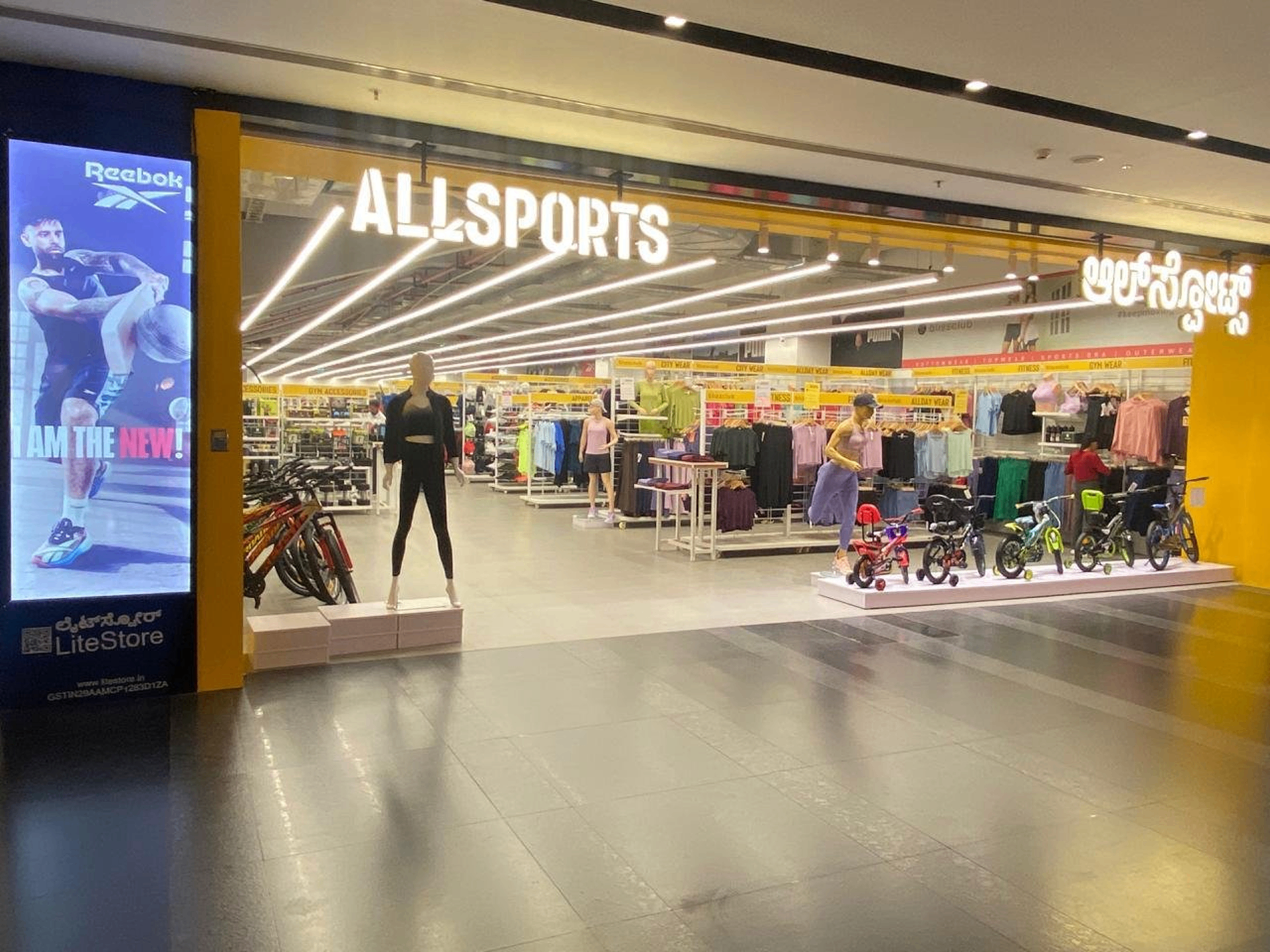 ALL SPORTS - Modern retail storefront in mall with illuminated signage, sports equipment displays, and customer shopping areas
